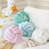 A collection of soft, round knitted velvet throw pillows in pastel shades including mint green, light blue, pink, and white.