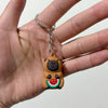 A small, round brown capybara charm with a green and red watermelon face is attached to a silver keyring.