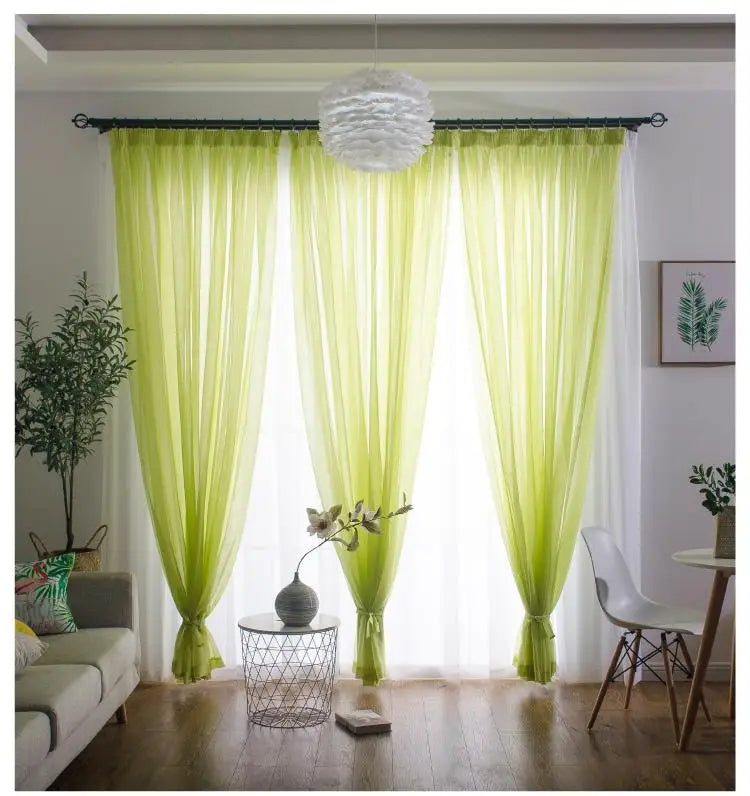 Light green sheer voile curtains hanging in a window with a dark rod pocket and white sheer fabric.