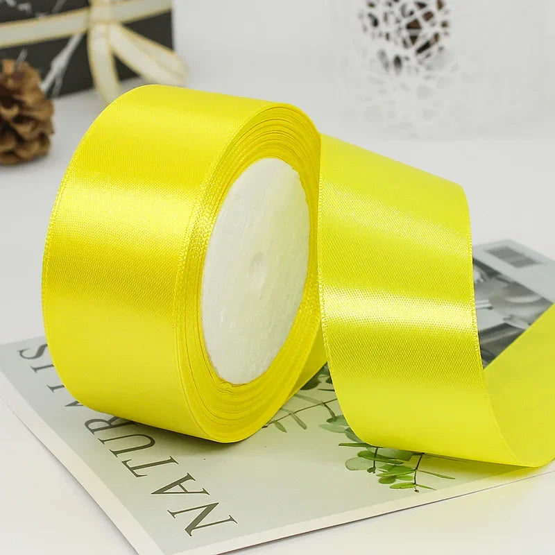 A roll of bright yellow satin ribbon used for gift wrapping or DIY crafts, lying on a piece of paper.