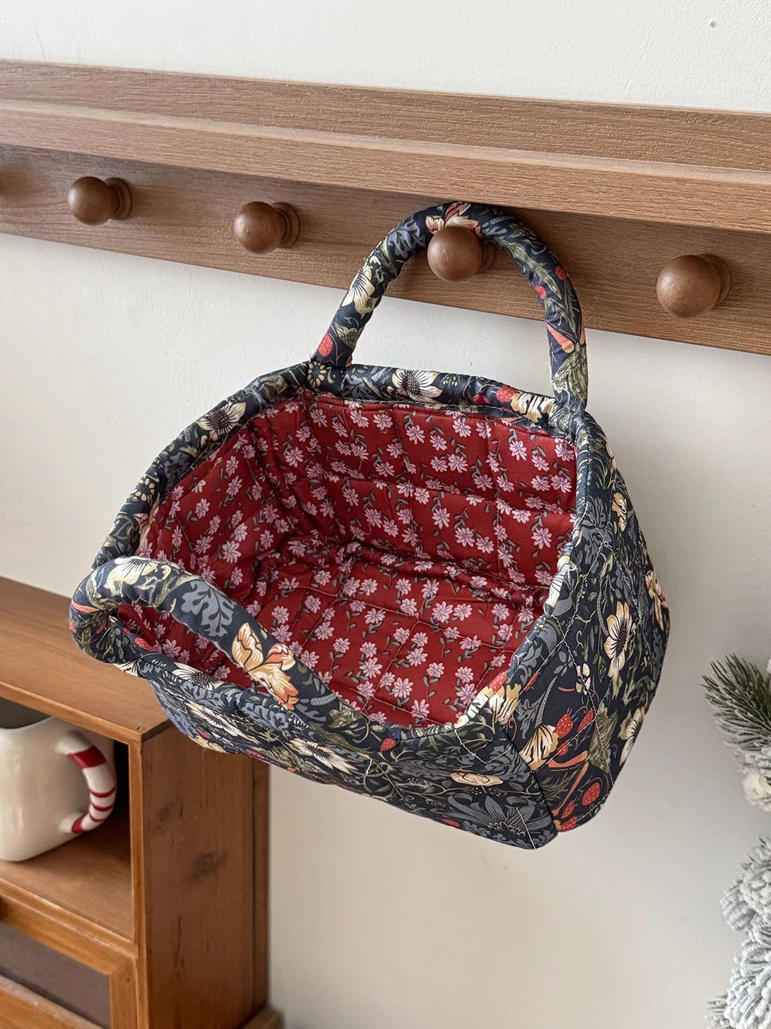 A dark floral patterned fabric storage basket with a woven handle is hanging on a wooden shelf.