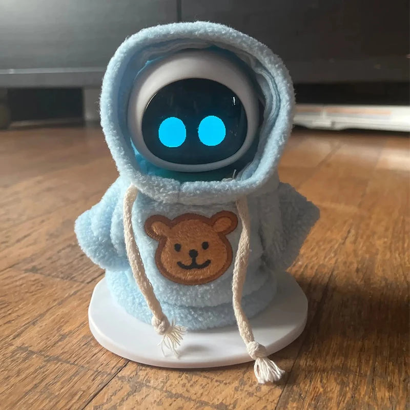 A cute robot plush toy wearing a light blue hooded outfit with a brown bear patch and glowing blue eyes.