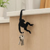 A black monkey-shaped wooden wall hook for keys and decor mounted on a light wood cabinet.