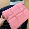 Rosa gesteppte Puffer-Laptoptasche mit Reißverschluss, von einer Hand gehalten auf dunkelblauem Jeansstoff.