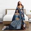 A woman wearing a blue patterned microfiber fleece throw blanket is lying on a bed.