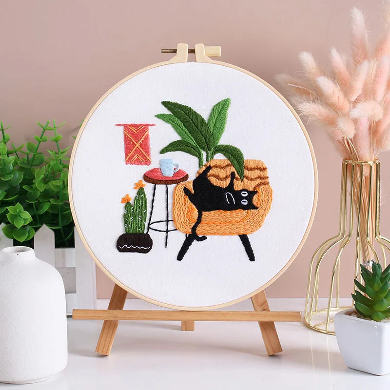 Embroidery kit featuring pre-printed floral and cat designs on white fabric displayed on a wooden easel.