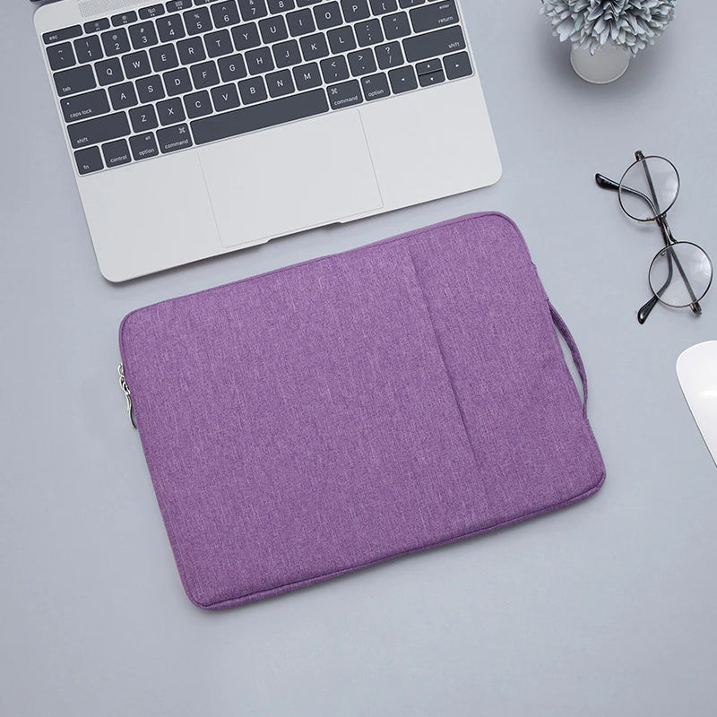 A purple waterproof laptop sleeve with a handle is shown next to a silver laptop and eyeglasses.