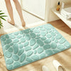A teal plush non-slip bathroom rug with a pebble texture placed on a wooden floor.