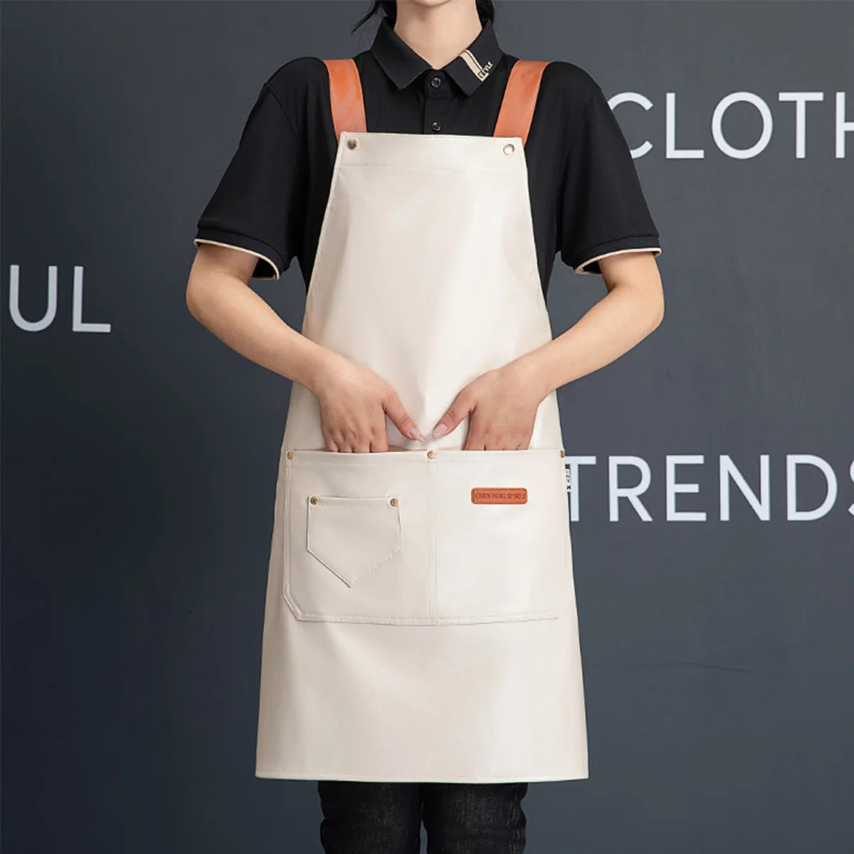 A person wearing a beige PU leather multi-pocket kitchen apron over a black shirt.