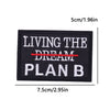 Black embroidered iron-on patch with white text reading LIVING THE DREAM PLAN B