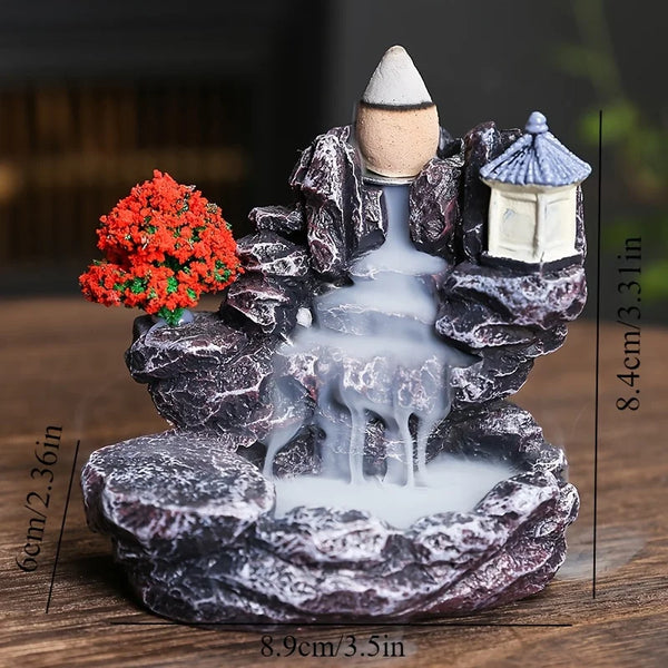 Escultura de roca gris oscura con una casita y una cascada de humo blanco, usada como quemador de incienso.