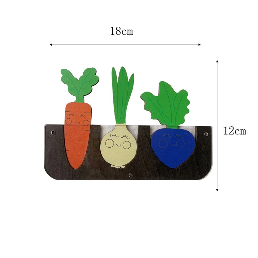 A wooden busy board featuring three vegetable shapes: a carrot, a leek, and a pea pod.