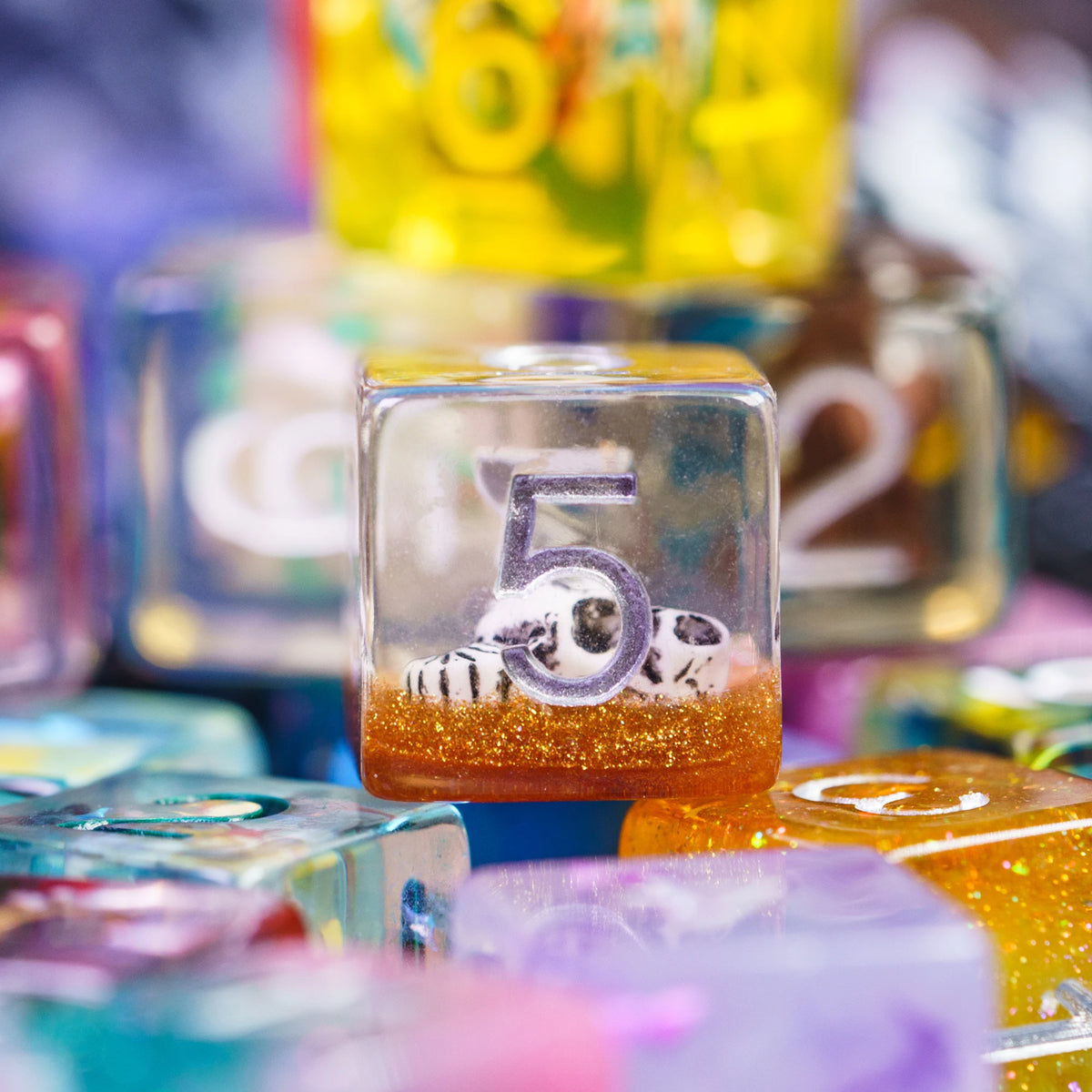 A close-up of a translucent orange resin die with gold glitter and a white and black marbled design.