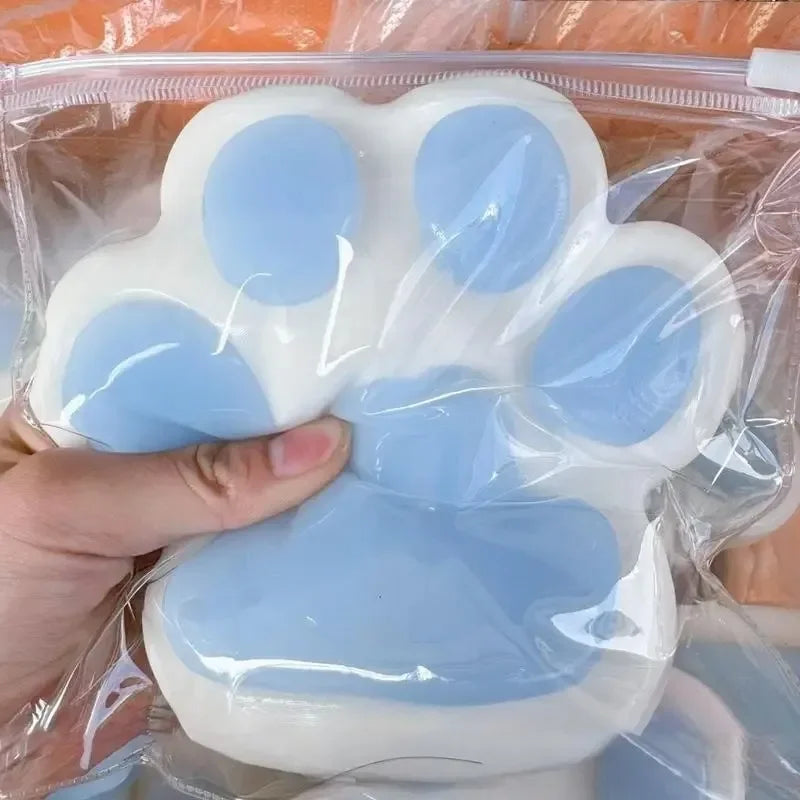 A hand is holding a white silicone cat paw squeeze toy with blue accents inside clear plastic packaging.