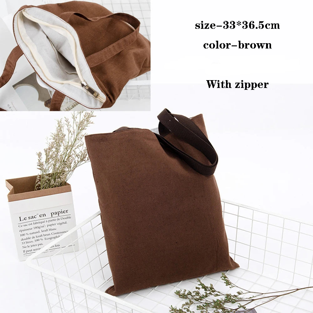 A brown canvas tote bag with a zipper is shown next to a small plant and a paper tag.