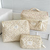 A beige floral quilted cosmetic bag is shown in various sizes resting on a white surface.