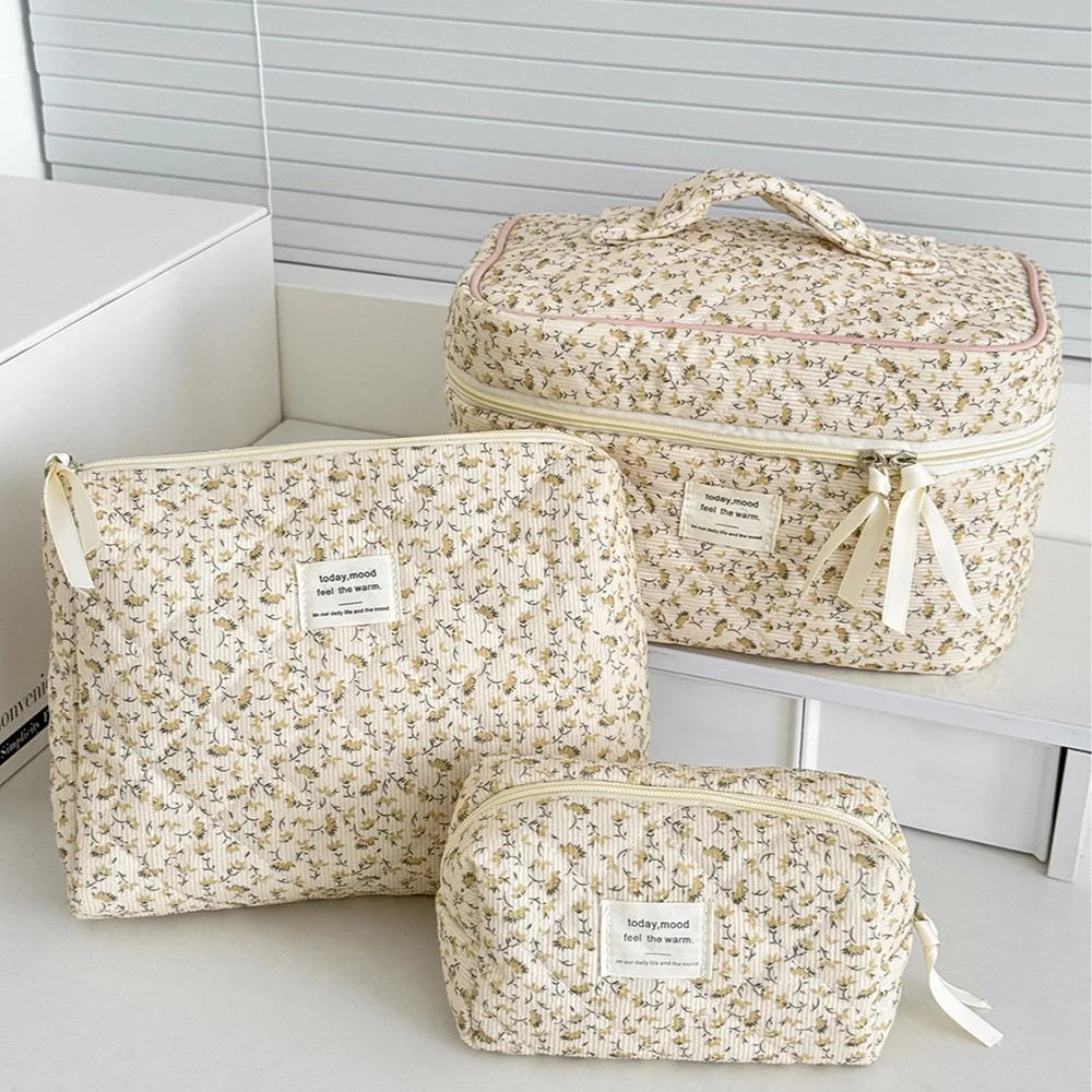 A beige floral quilted cosmetic bag is shown in various sizes resting on a white surface.
