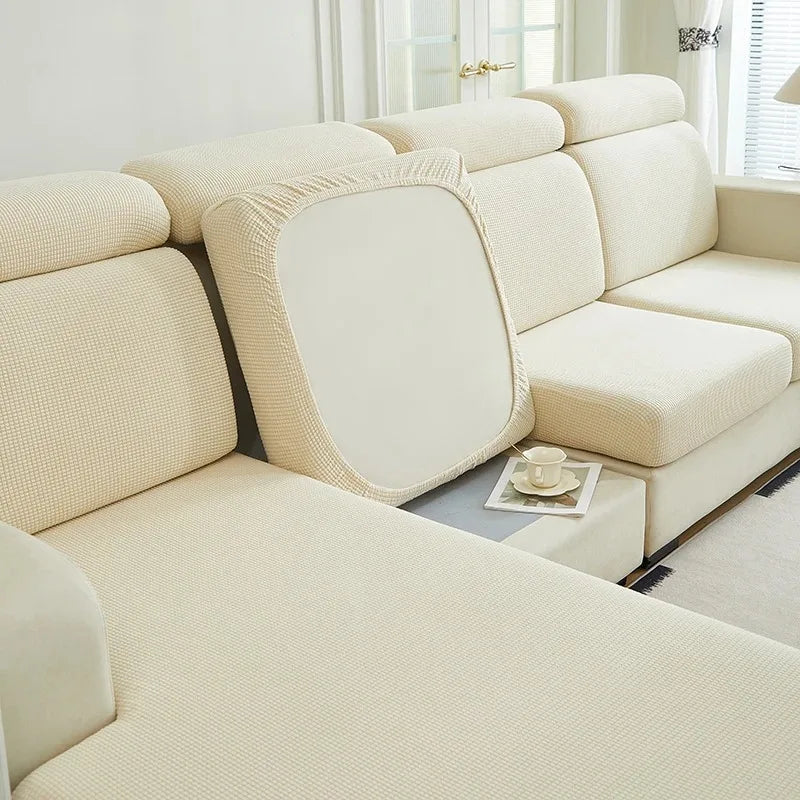 A cream-colored stretch sofa slipcover with a textured fabric and light wood accents in a bright room.