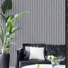 A potted green plant next to a black leather sofa with white pillows against a gray vertical striped wall.