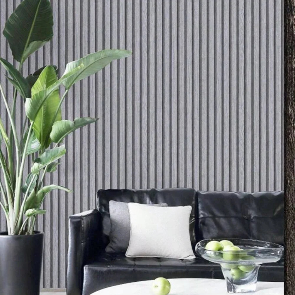 A potted green plant next to a black leather sofa with white pillows against a gray vertical striped wall.