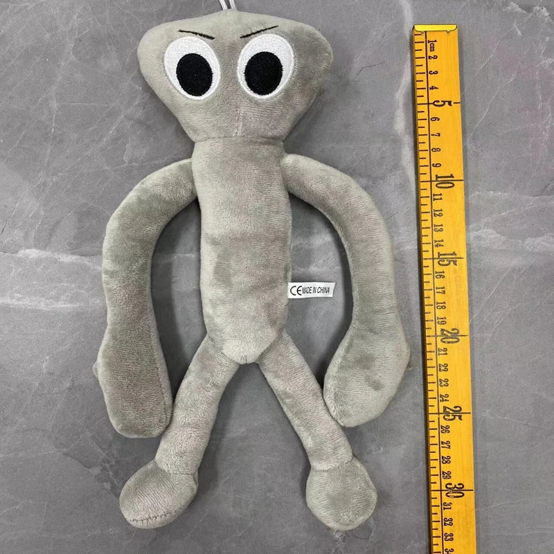 A gray plush toy resembling a bird with large white eyes and long limbs, shown next to a yellow ruler.