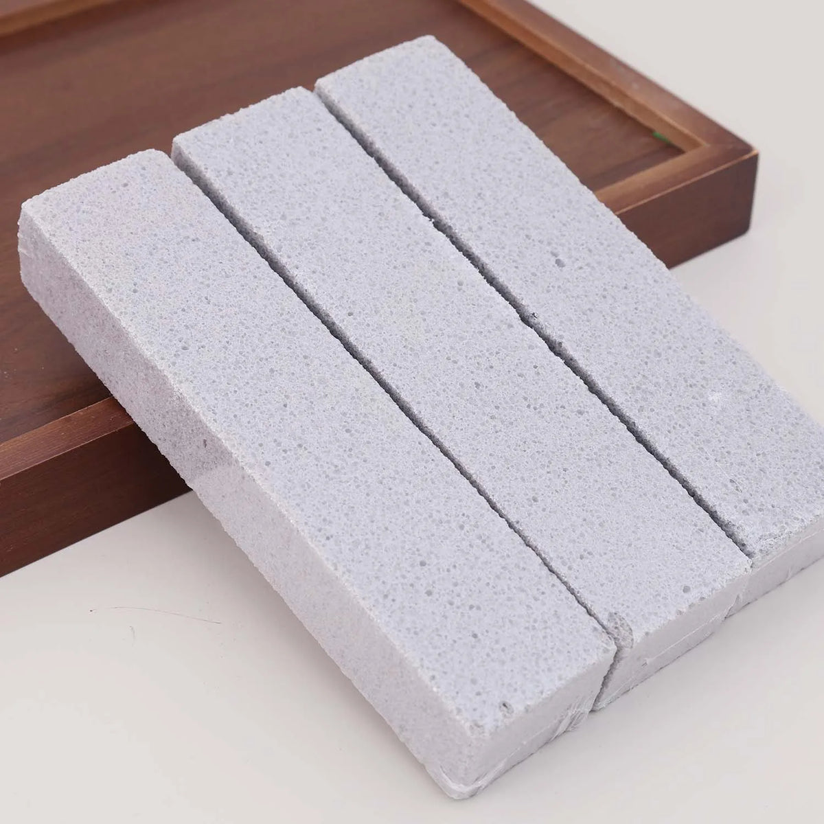 Three rectangular white foam glass pumice stone cleaning brushes resting on a wooden tray