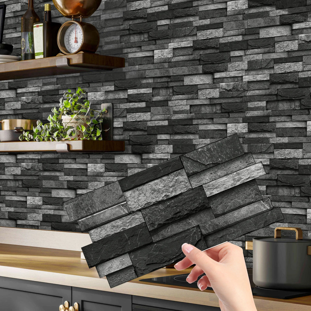 A hand is placing peel and stick waterproof tile stickers on a dark gray stone backsplash in a kitchen setting.