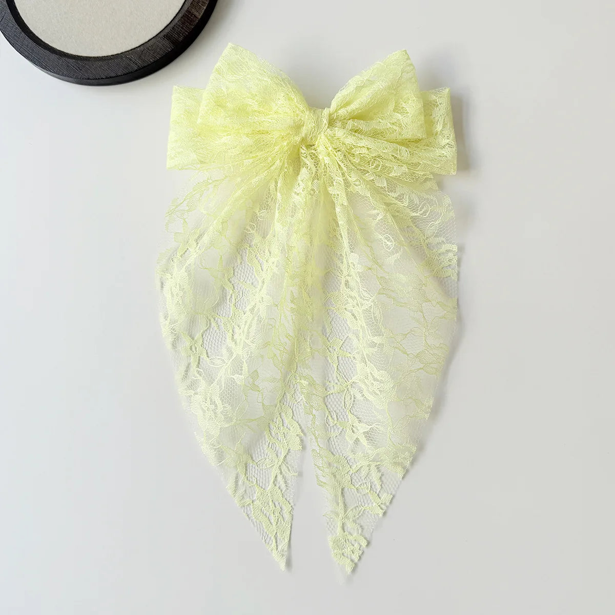 A pale yellow lace bow accessory for hair, featuring delicate floral patterns.