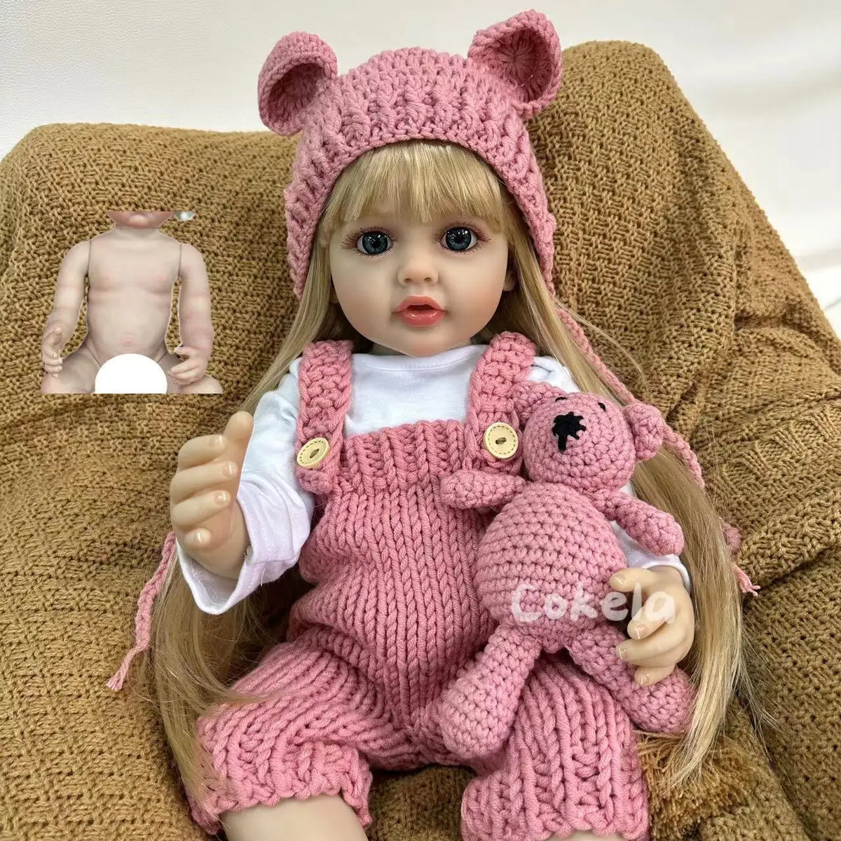 A lifelike silicone baby doll wearing a pink knitted outfit and a matching hat, sitting on a brown textured surface.