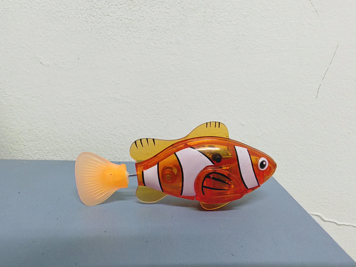 An orange and white light-up sensor swimming fish toy with a translucent yellow fin.