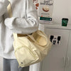 A light beige canvas travel tote bag with a tan crossbody strap is shown next to a person's torso.
