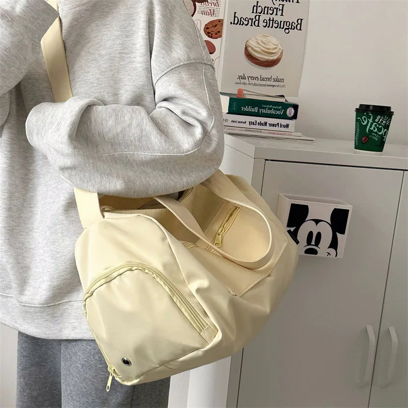 A light beige canvas travel tote bag with a tan crossbody strap is shown next to a person's torso.