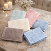 A stack of soft, pastel-colored organic cotton face towels in shades of pink, mint green, beige, and blue on a marble surface