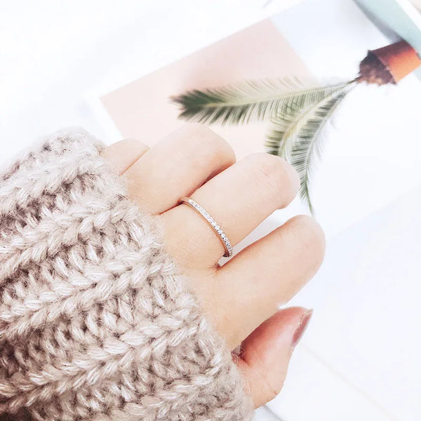A hand wearing an adjustable sterling silver zircon ring, resting on a white surface with a pink card and a green feather.