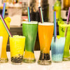 A collection of colorful juice drinks in glasses, garnished with reusable stainless steel drinking straws.