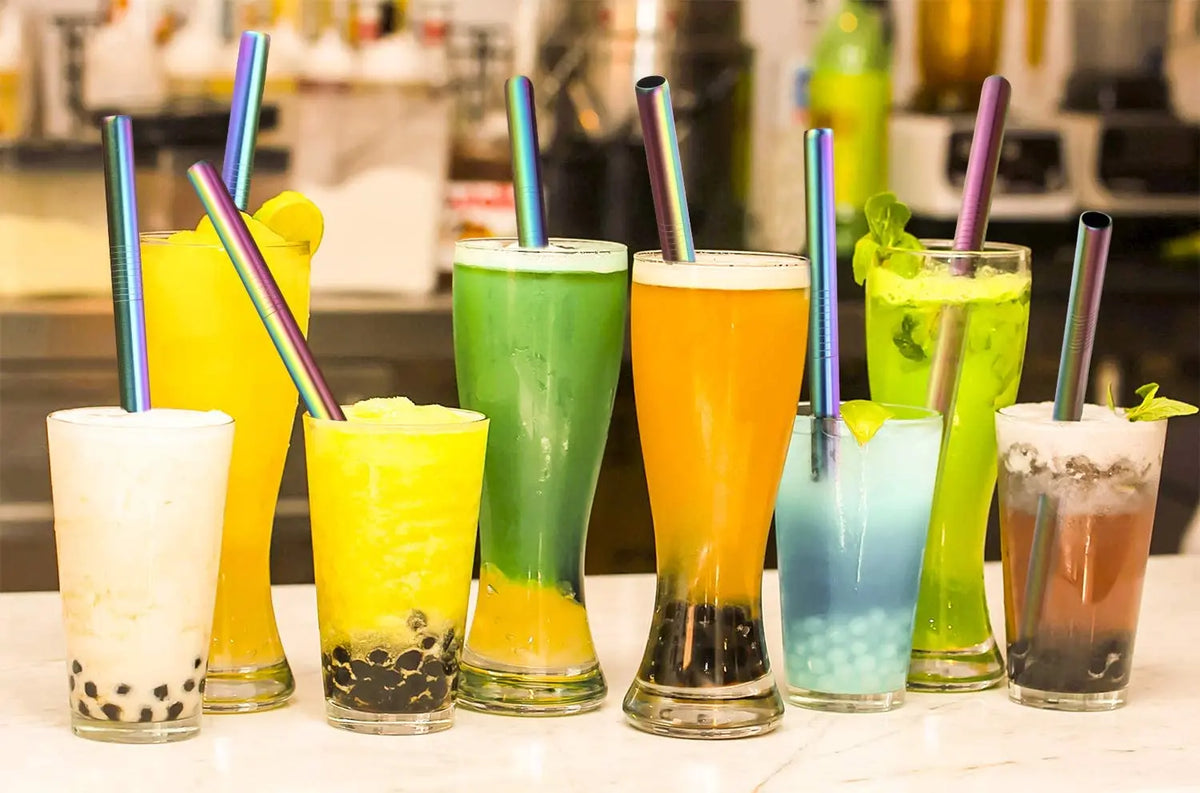 A collection of colorful juice drinks in glasses, garnished with reusable stainless steel drinking straws.