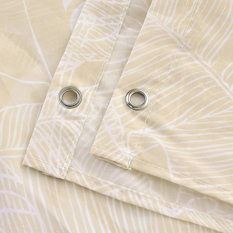 Close-up of a light beige shower curtain fabric with a white leaf pattern and silver grommets.