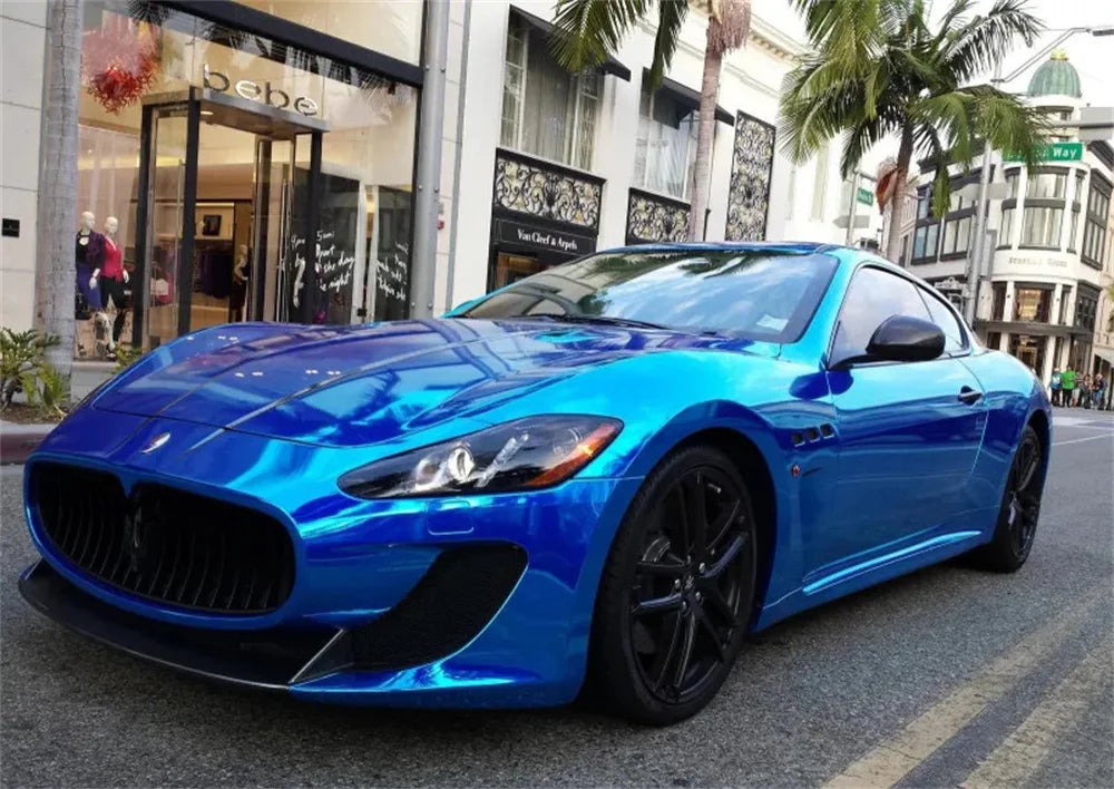 A bright blue muscle car with a glossy chrome mirror wrap parked on a city street.