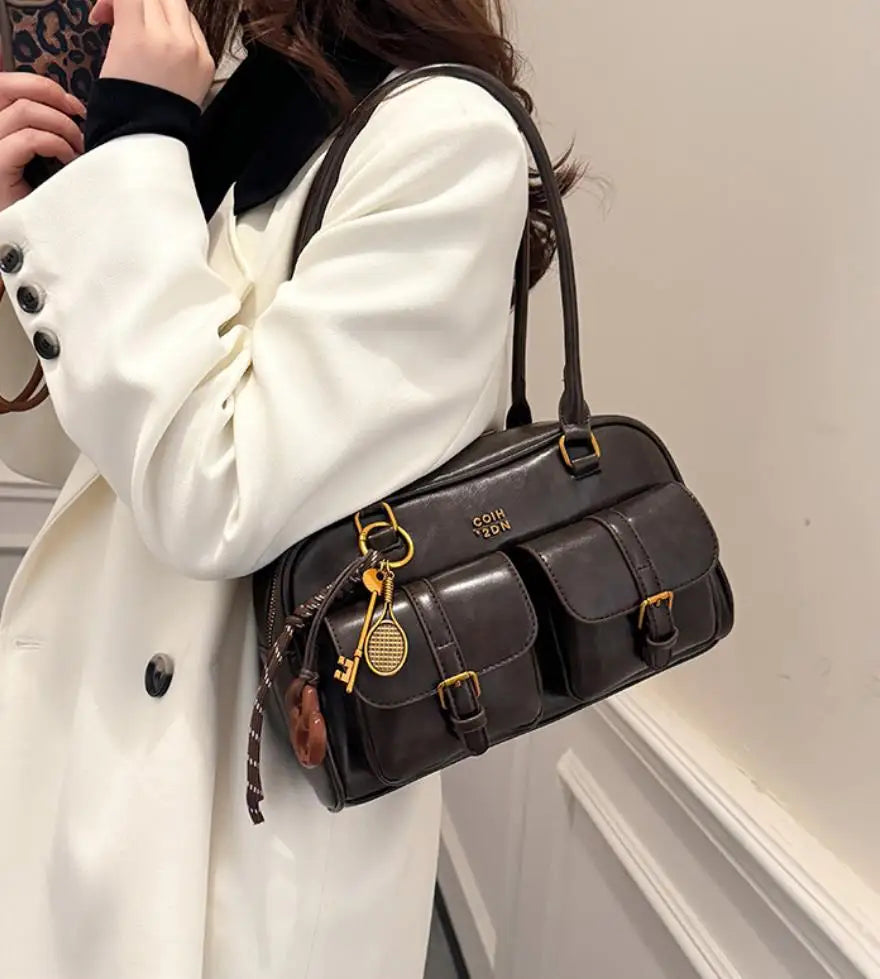 Eine Frau hält eine braune Handtasche mit vielen Fächern vor einem weißen Mantel.