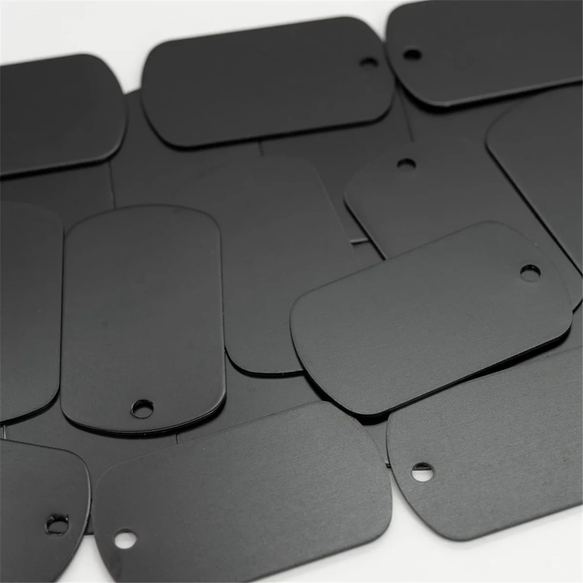 A collection of black aluminum stamping dog tags arranged on a white surface.