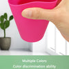 A hand holds a bright pink plastic cup designed for a color discrimination game.