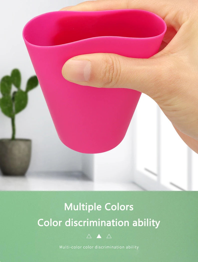 A hand holds a bright pink plastic cup designed for a color discrimination game.
