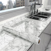 A stainless steel kitchen sink and faucet installed in a white marble countertop with a long marble effect film rolled out.