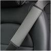 A close-up of a gray PU leather embossed seat belt shoulder cushion on a dark car seat.