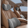 A close-up view of a tan car seat headrest with a gray memory foam pillow providing lumbar support.