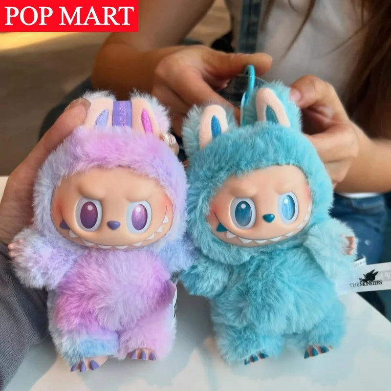 A pair of Labubu Big Into Energy plush dolls, one purple and one blue, are being held by a person.