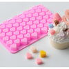 A pink silicone mold tray filled with small heart-shaped silicone molds and a finished cake decorated with pink frosting and 