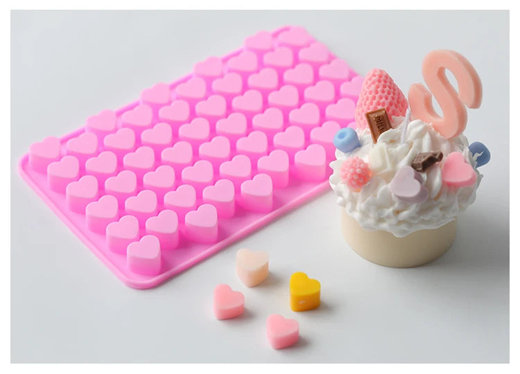 A pink silicone mold tray filled with small heart-shaped silicone molds and a finished cake decorated with pink frosting and 