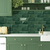 A kitchen backsplash featuring dark green subway tiles above a white countertop and cabinet.
