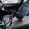 A black pistol-shaped keychain set with multiple keys rests on a dark car seat.